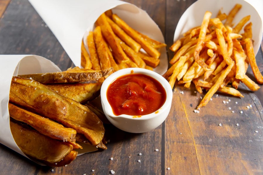 three cones of fries with ketchup on a wooden table