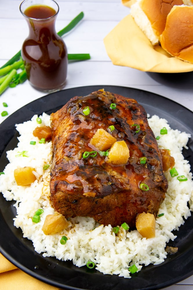 a black platter with white rice, pineapple, and a cooked glazed pork loin 