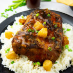 a black platter with rice and pineapple chunks around a roasted pork loin