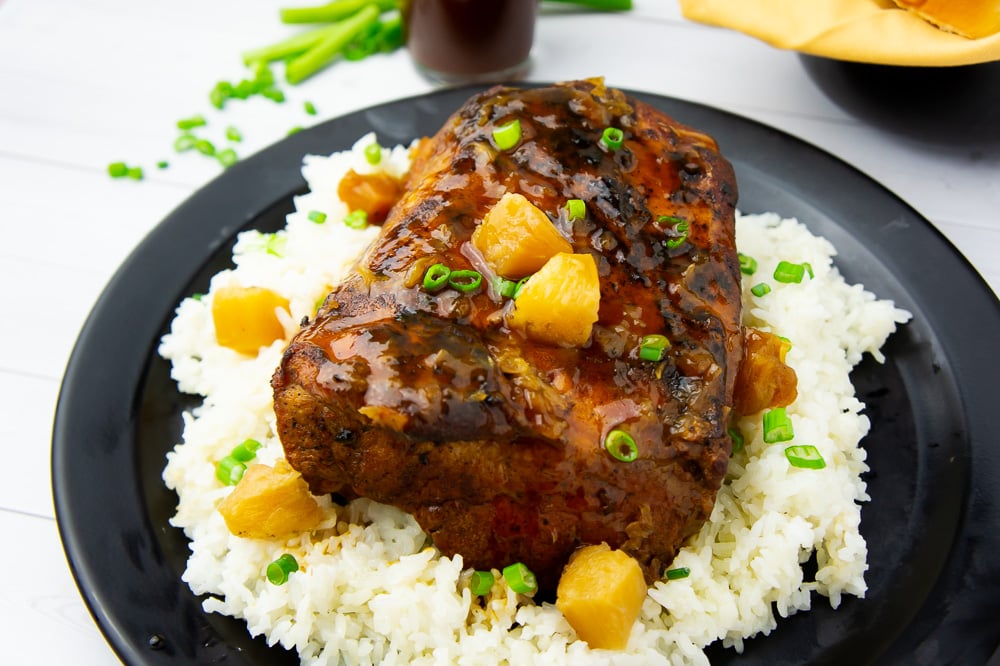 a black platter with rice and pineapple chunks around a roasted pork loin
