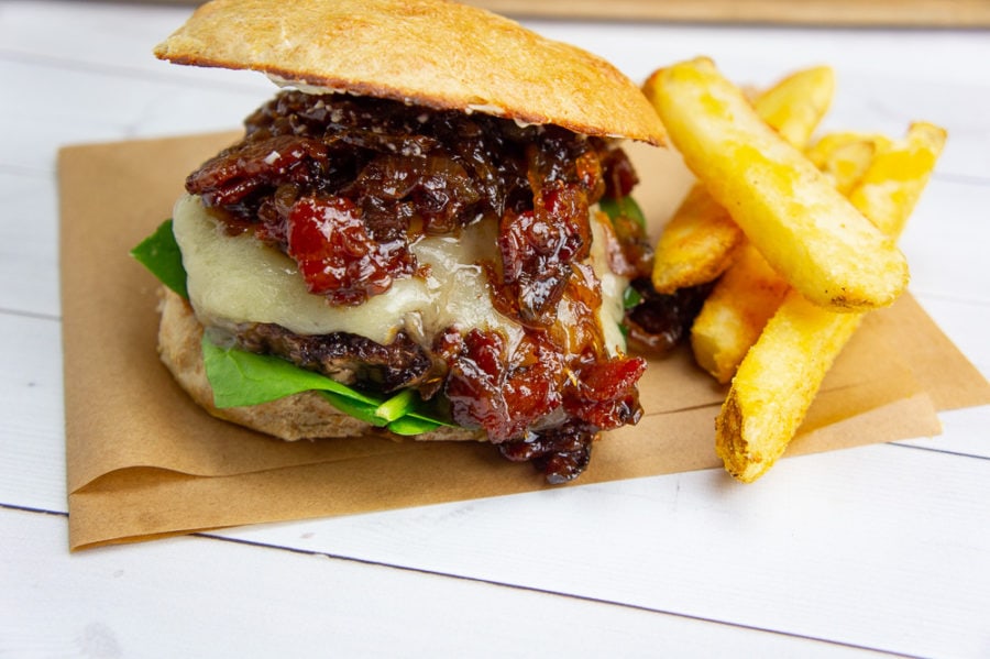 a bacon jam burger on a parchment square with french fries on a white wooden table