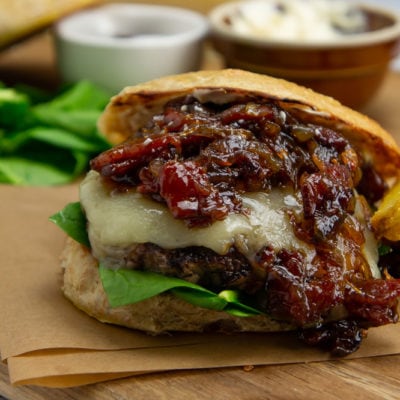 a wooden cutting board with a bacon onion jam burger, fries, a bowl of mayo and fresh spinach