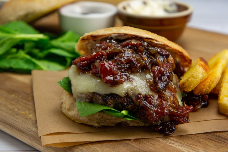 a wooden cutting board with a bacon onion jam burger, fries, a bowl of mayo and fresh spinach
