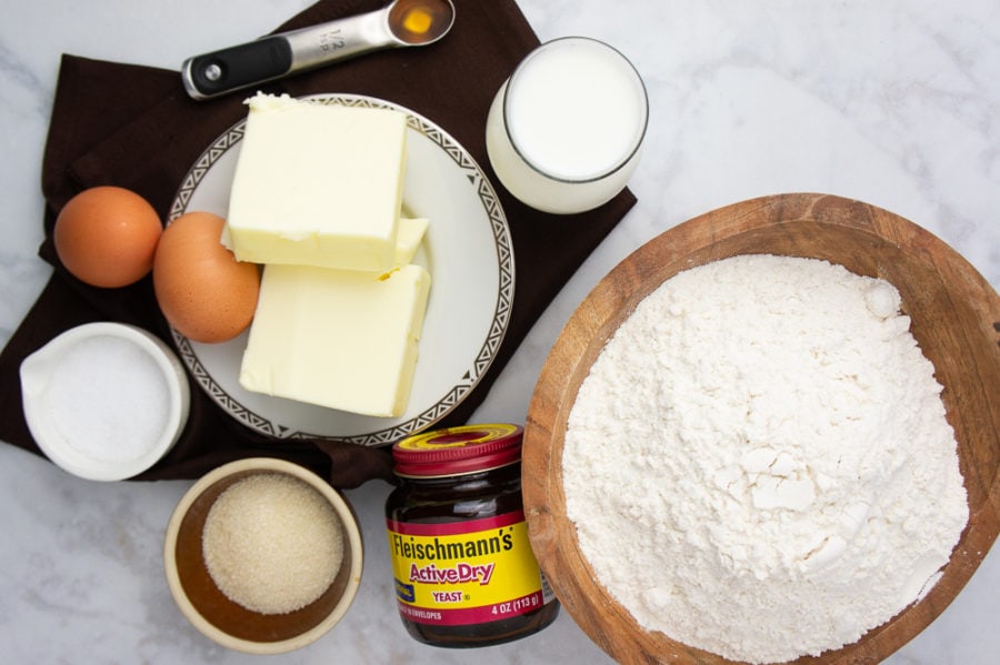 a big bowl of flour with butter, cream cheese, eggs, milk, and yeast beside it