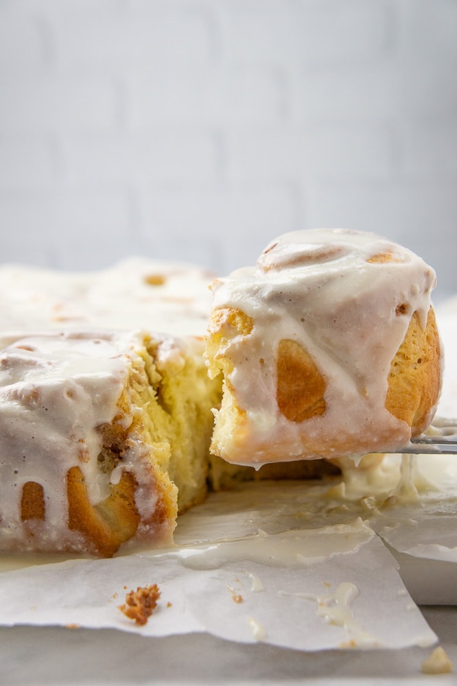 cream cheese cinnamon rolls on parchment paper with one being lifted away with a spatula