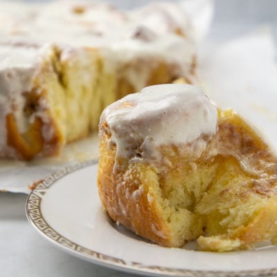 a cream cheese cinnamon roll set on a plate in front of the rest of the cinnamon rolls