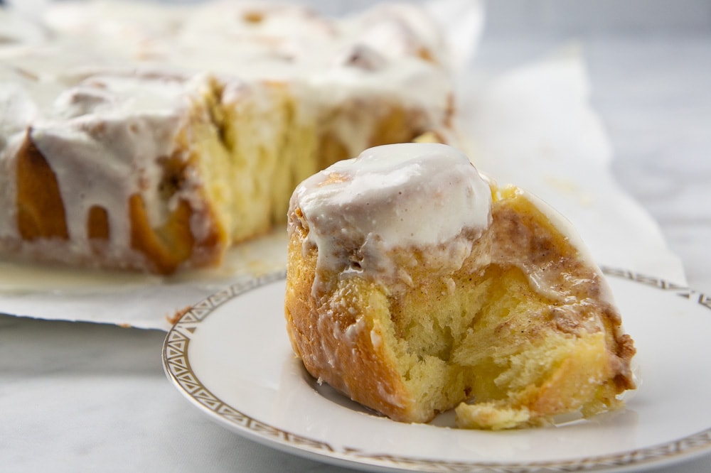 a cream cheese cinnamon roll set on a plate in front of the rest of the cinnamon rolls