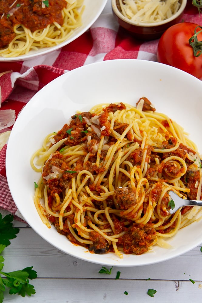 a bowl of pasta with meat tomato sauce in a white bowl