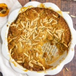 a white pie plate with baked loquat cobbler with a white towel beside it