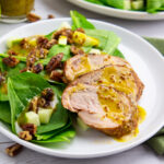 three slices of pork tenderloin with spinach, apples, and pecans, drizzled with a yellow, whole grain mustard vinaigrette.