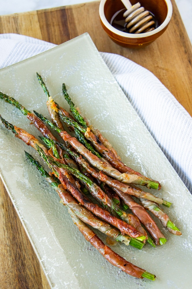 a platter of prosciutto wrapped asparagus with a wooden cutting board and white linen towel