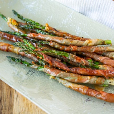 a platter of grilled prosciutto wrapped asparagus on a wooden cutting board