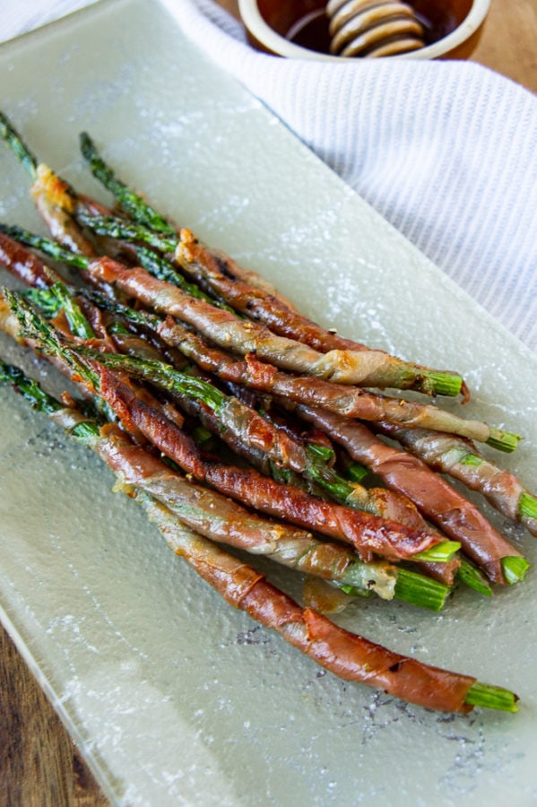a platter of prosciutto wrapped asparagus with a wooden cutting board and white linen towel