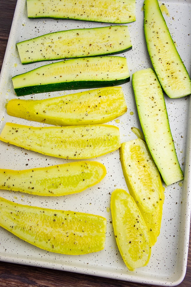 a white baking sheet with slices of summer squash seasoned with salt and pepper