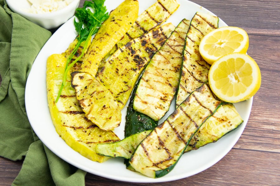 a white platter of grilled summer squash with a sliced lemon