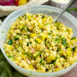 a frosted glass bowl with summer squash pasta salad on a wooden table beside a green linen towel
