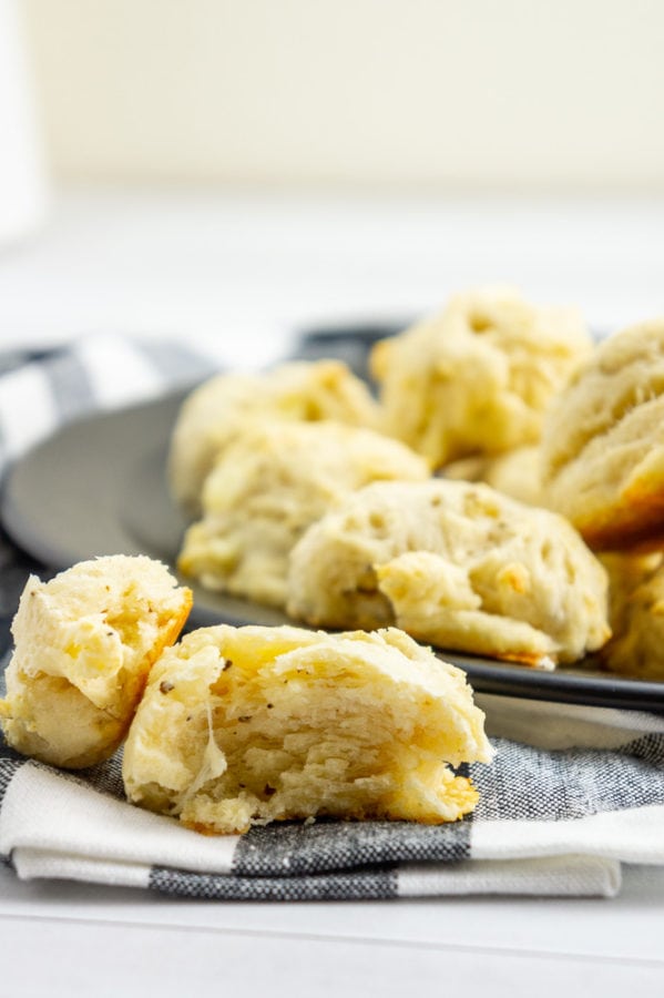 a cut open asiago biscuit on a black and white checkered linen napkin with more biscuits on a black plate