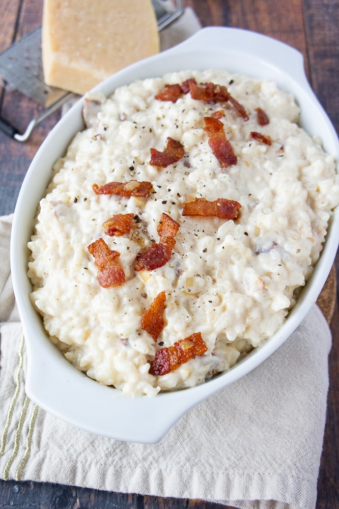 an oval white dish with creamy cheesy rice in it topped with bacon