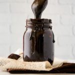 a jar of fudge sauce with a spoon lifting fudge out