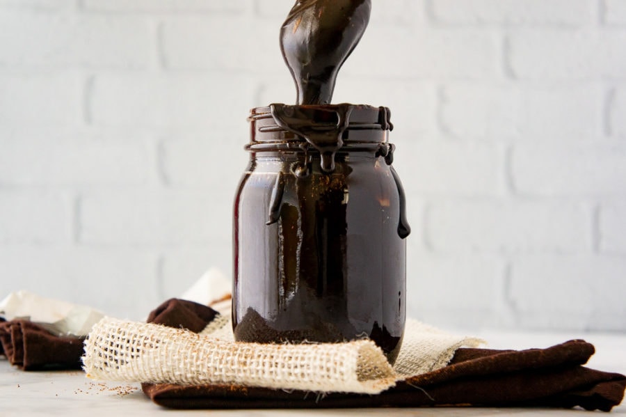 a jar of fudge sauce with a spoon lifting fudge out