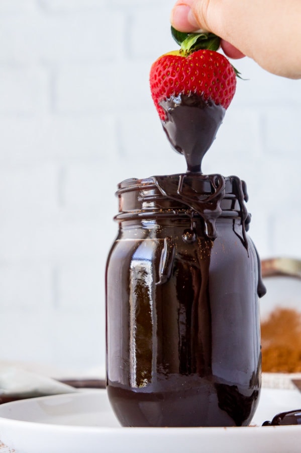 a jar of fudge sauce with a strawberry dipped in