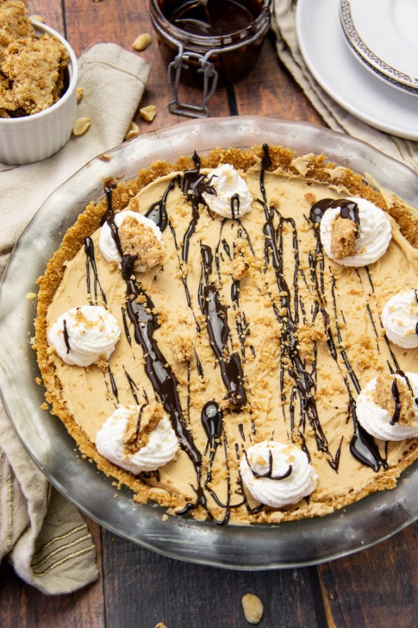 a peanut butter pie with chocolate sauce and whipped cream in a glass pie plate