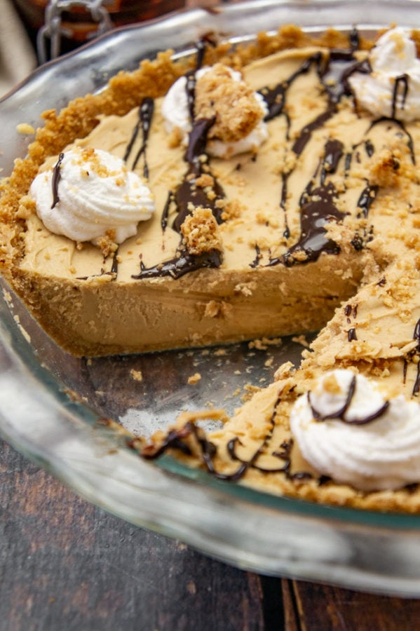 a close up of frozen peanut butter pie in a glass pie plate with a slice removed