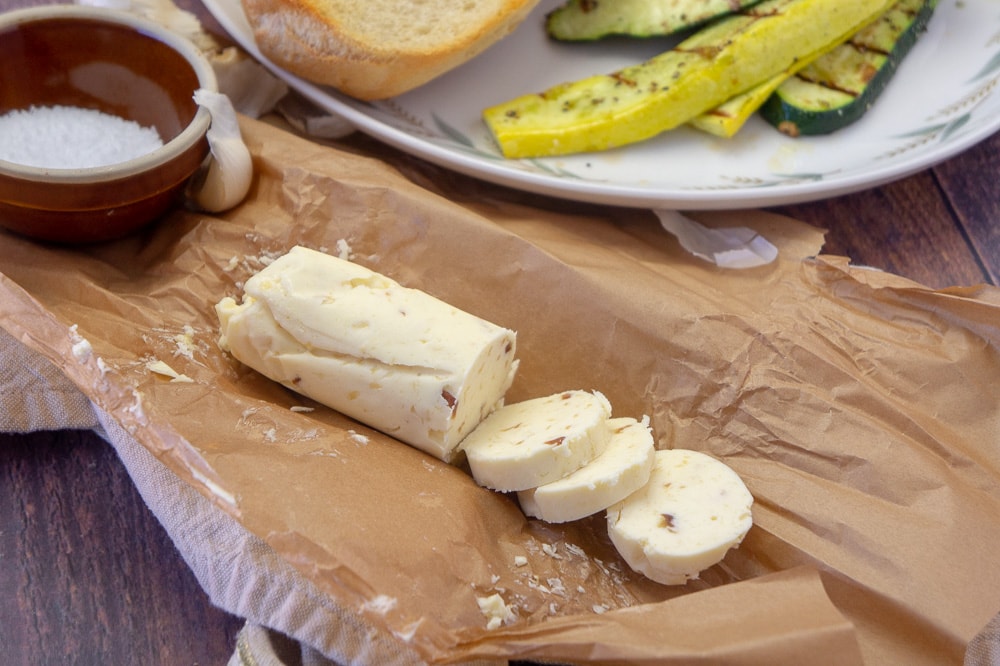 A sliced log of garlic compound butter on parchment paper