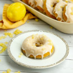 a small plate with a single donut on it in front of a tray of donuts and a lemon