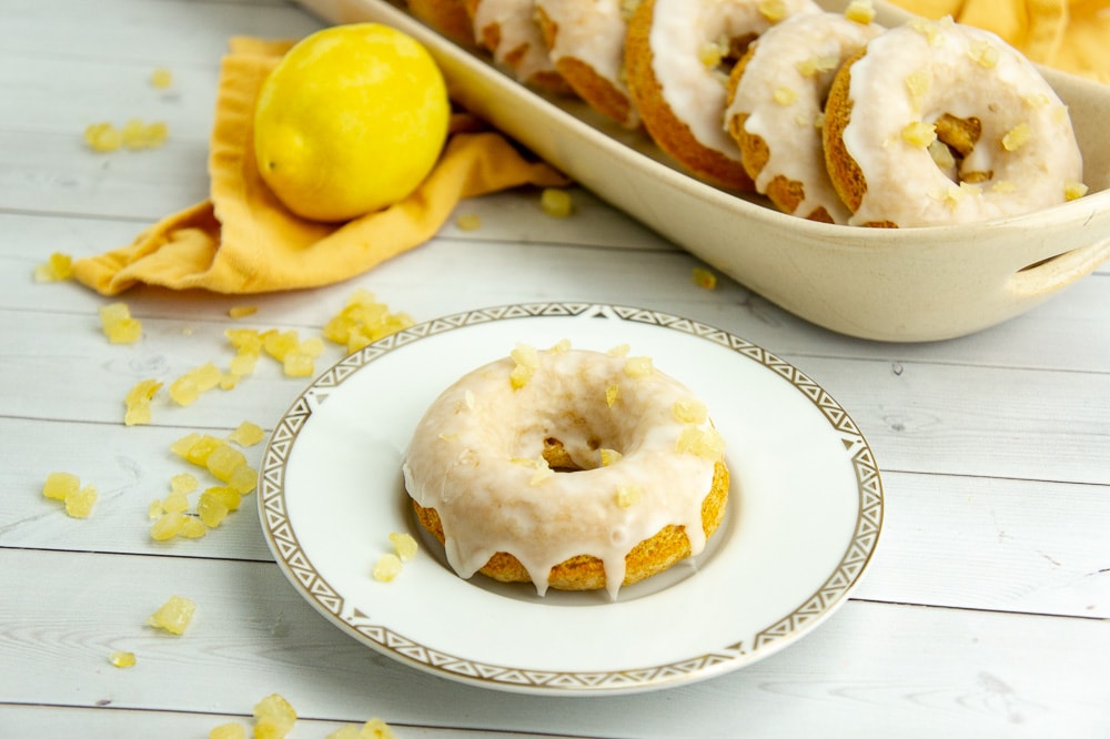 a small plate with a single donut on it in front of a tray of donuts and a lemon