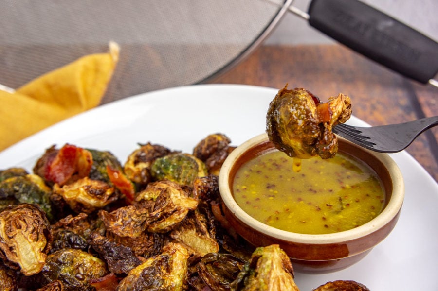 a deep fried brussels sprout on a fork being dipped in a mustard sauce