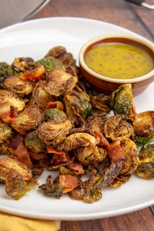 a white platter with deep fried brussels sprouts with a brown bowl of yellow mustard dressing