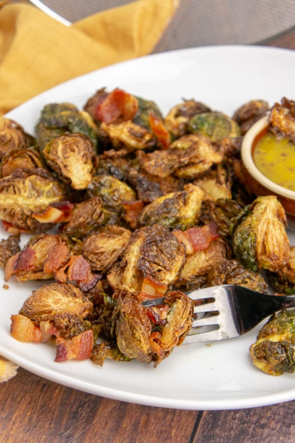 A fork stabbing a brussels sprout and bacon on a white platter 