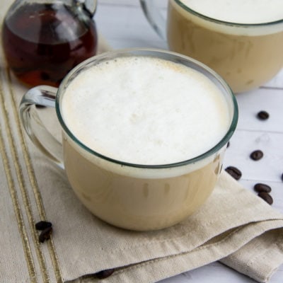 a creamy homemade latte in a glass cup on a beige napkin