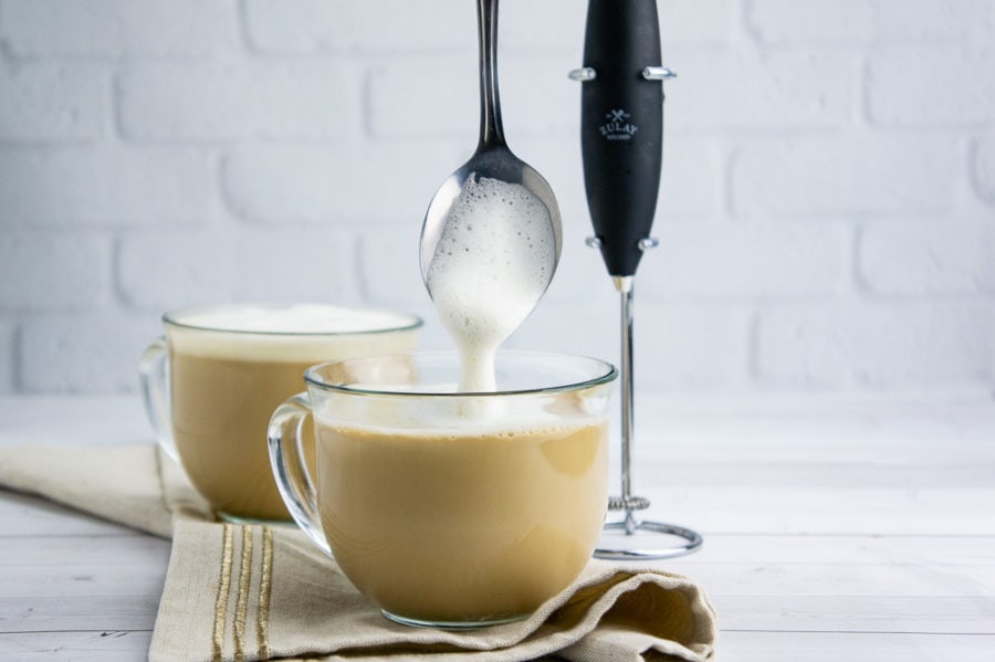 foam being ladled into a clear glass coffee cup with a latte in it