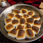 a pan with oven s'mores dip on a wood surface with a red and black checked napkin