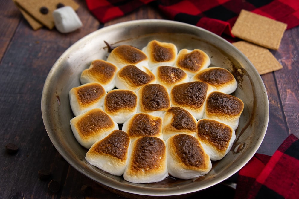 a pan with oven s'mores dip on a wood surface with a red and black checked napkin