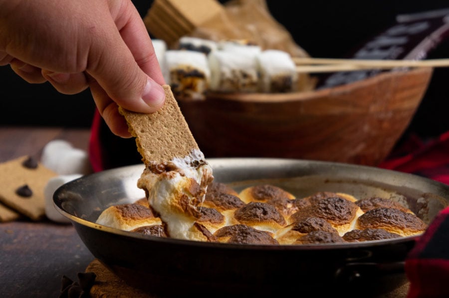 a graham cracker dipping into melted chocolate and gooey marshmallow