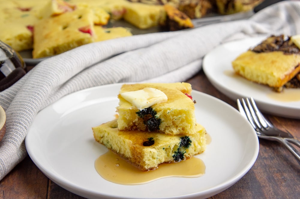 two baked pancake squares on a white plate with butter and syrup