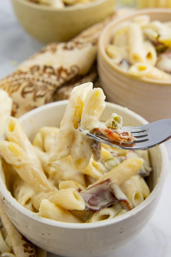 a fork lifting a bite of mac and cheese from a beige bowl