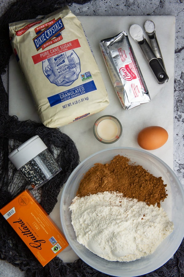 Ingredients for bat sugar cookies - sugar, egg, flour, cocoa powder, shortening, spinrkles and chocolate