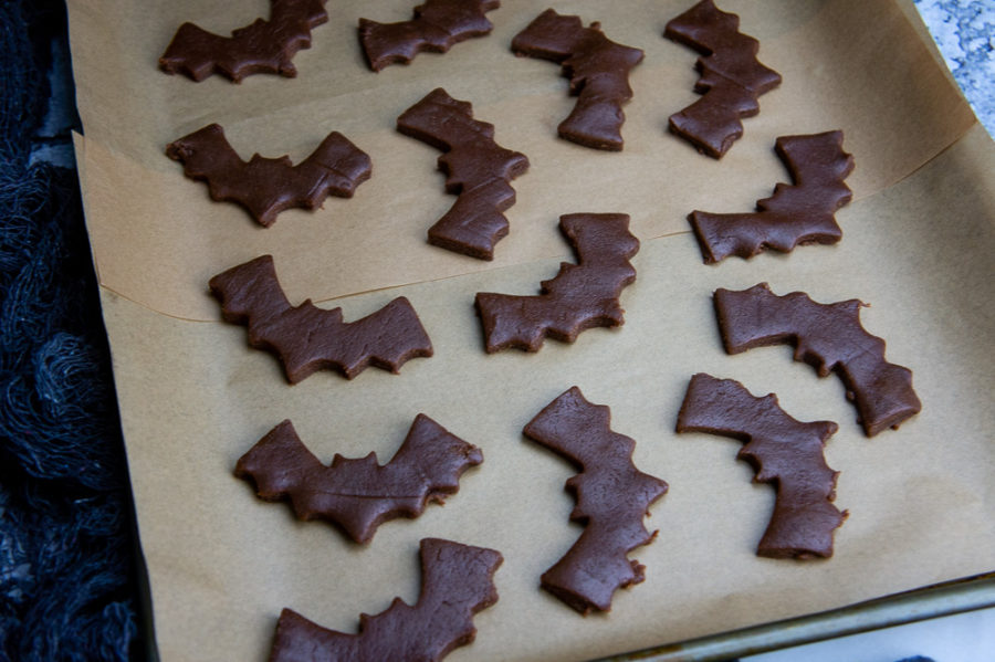 A baking sheet with parchment paper and cut out chocolate bat sugar cookies