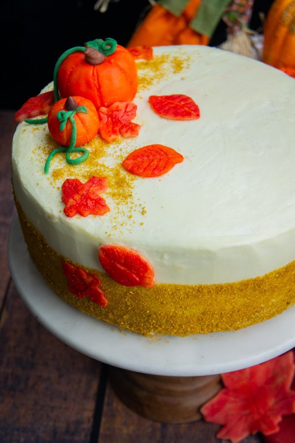 a decorated white frosted pumpkin layer cake with marzipan pumpkins and leaves and gold sprinkles