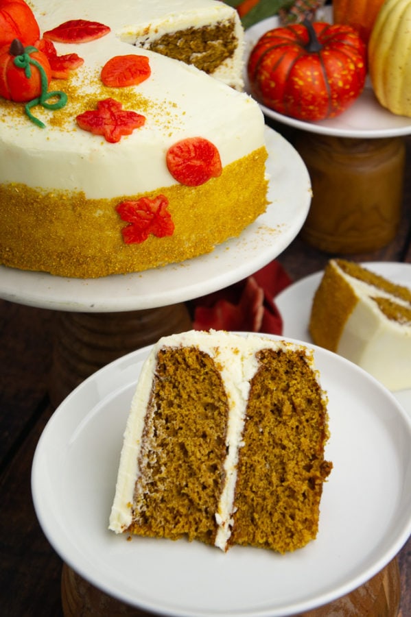 a two layer decorated pumpkin layer cake with a slice set on a white plate