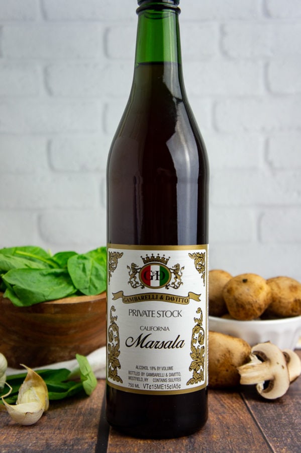 a bottle of marsala wine in front of bowls of spinach and mushrooms