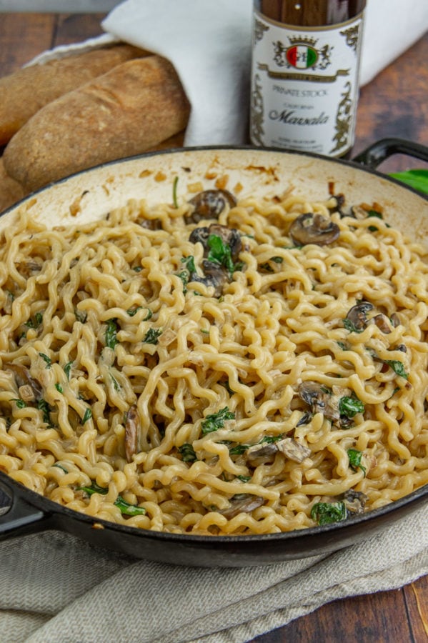 a black pot of pasta with marsala cream sauce next to baguettes