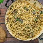 a large pot of wavy noddles with mushrooms and spinach in a creamy sauce beside some baguettes