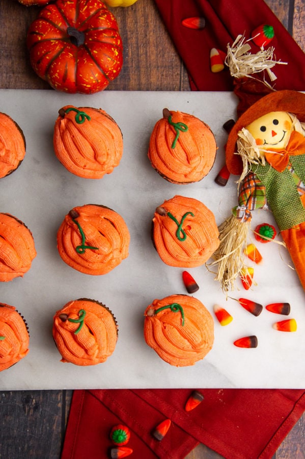 pumpkin cupcakes on a white granite slab with candy corn and a scarecrow