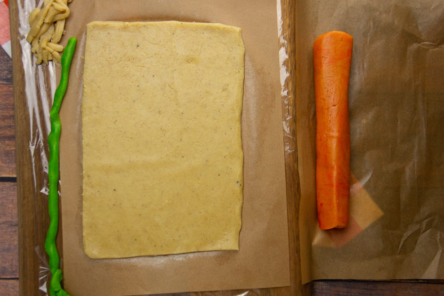 a sheet of dough with a log of orange dough and a strip of green dough beside it