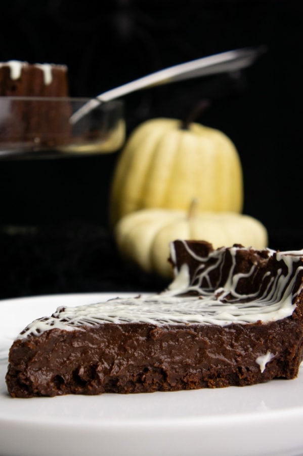 a slice of chocolate tart on a white plate in front of two pumpkins